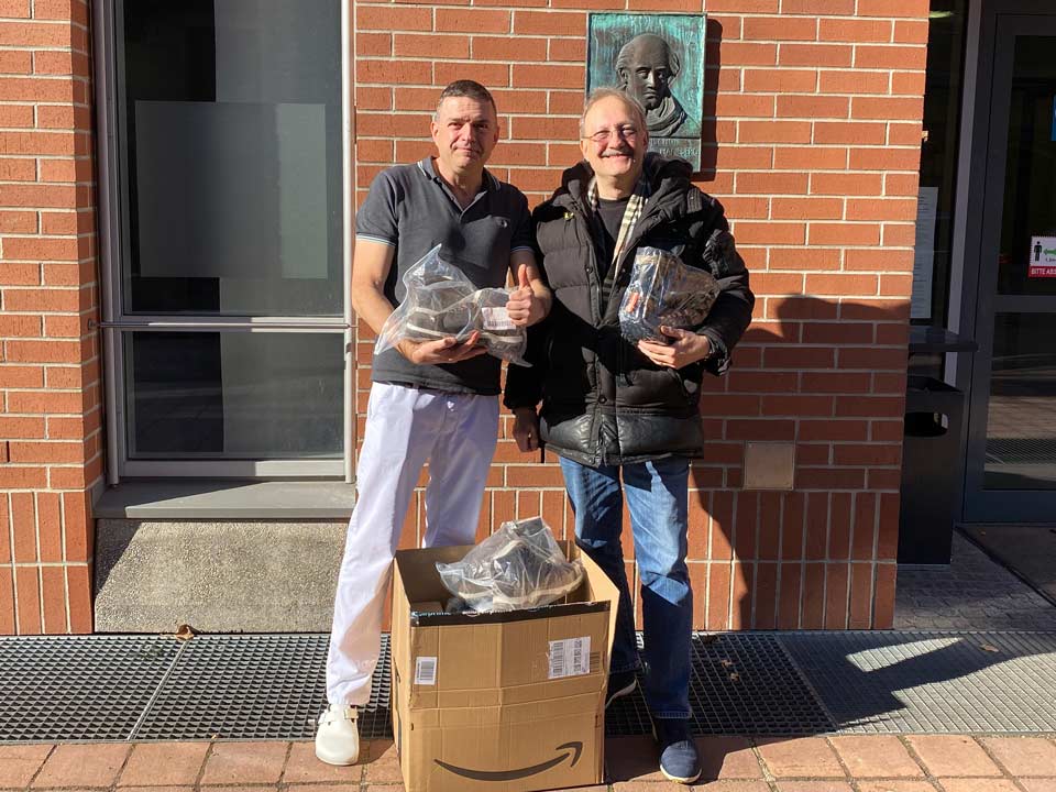 Dr. Ralf Ebersperger übergibt einen großen Karton mit neuen Winterschuhen an einen Mitarbeiter der Obdachlosenhilfe St. Bonifaz.